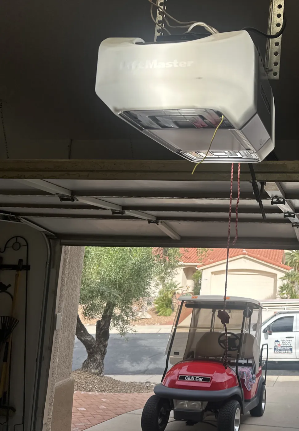 Golf cart parked under an open garage door with the opener overhead