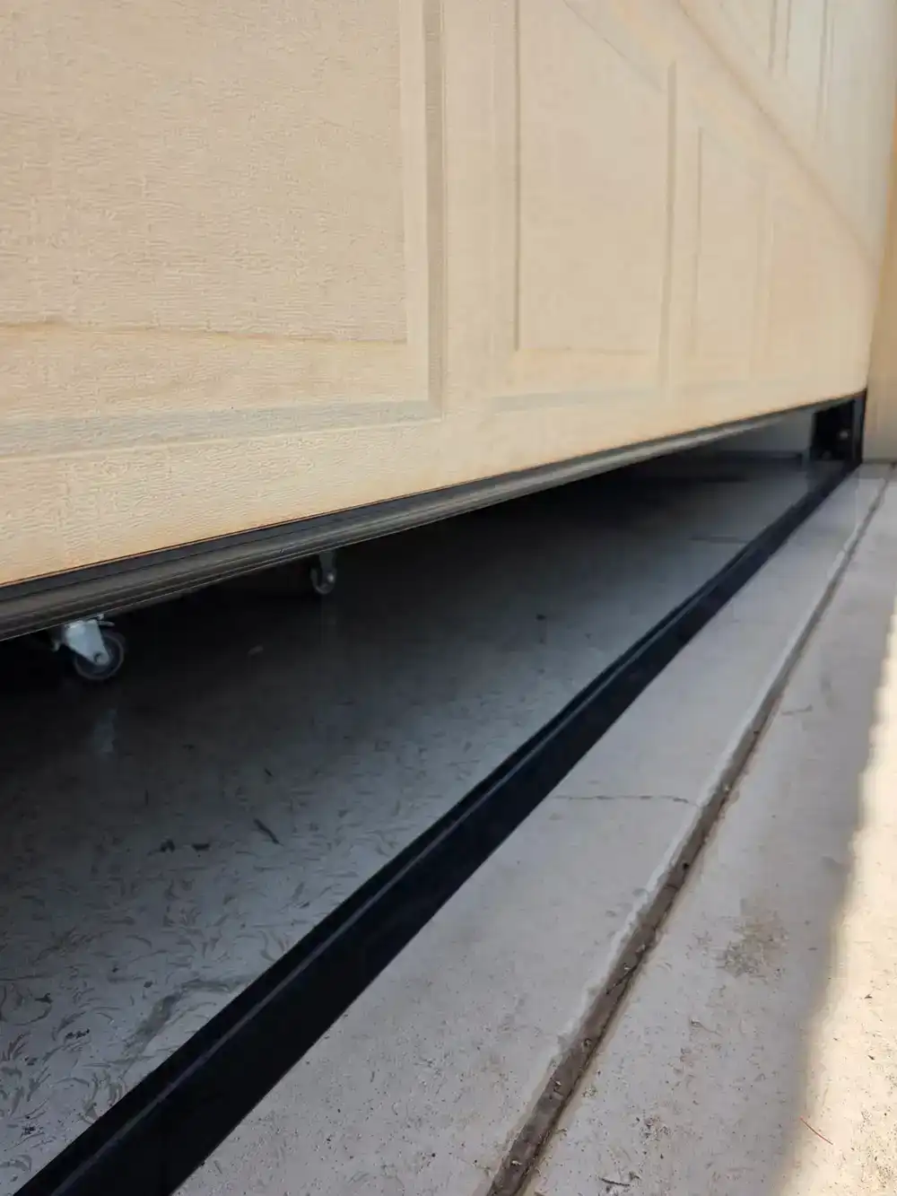 Bottom edge of a garage door panel with rollers visible above the track in a Tucson garage